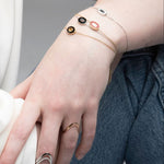 Hand wearing gold bracelets with small ceramic charms on a neutral background