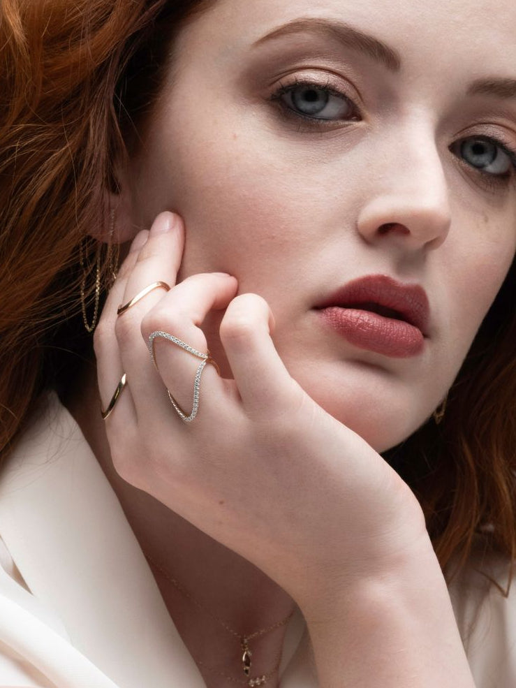 Woman wearing pave sculptural wave rings with a neutral background