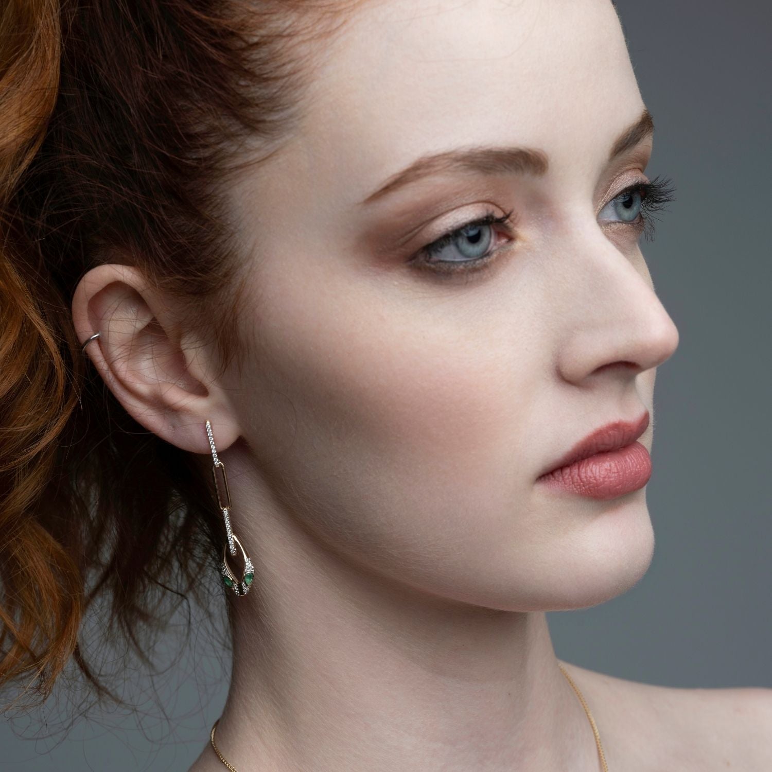 Woman wearing 14k gold serpent chain drop earrings with emerald eyes from Inessa Renewal Collection