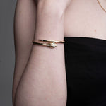 Close-up of 14k gold serpent hinged bangle with emerald eyes and diamond details on wrist