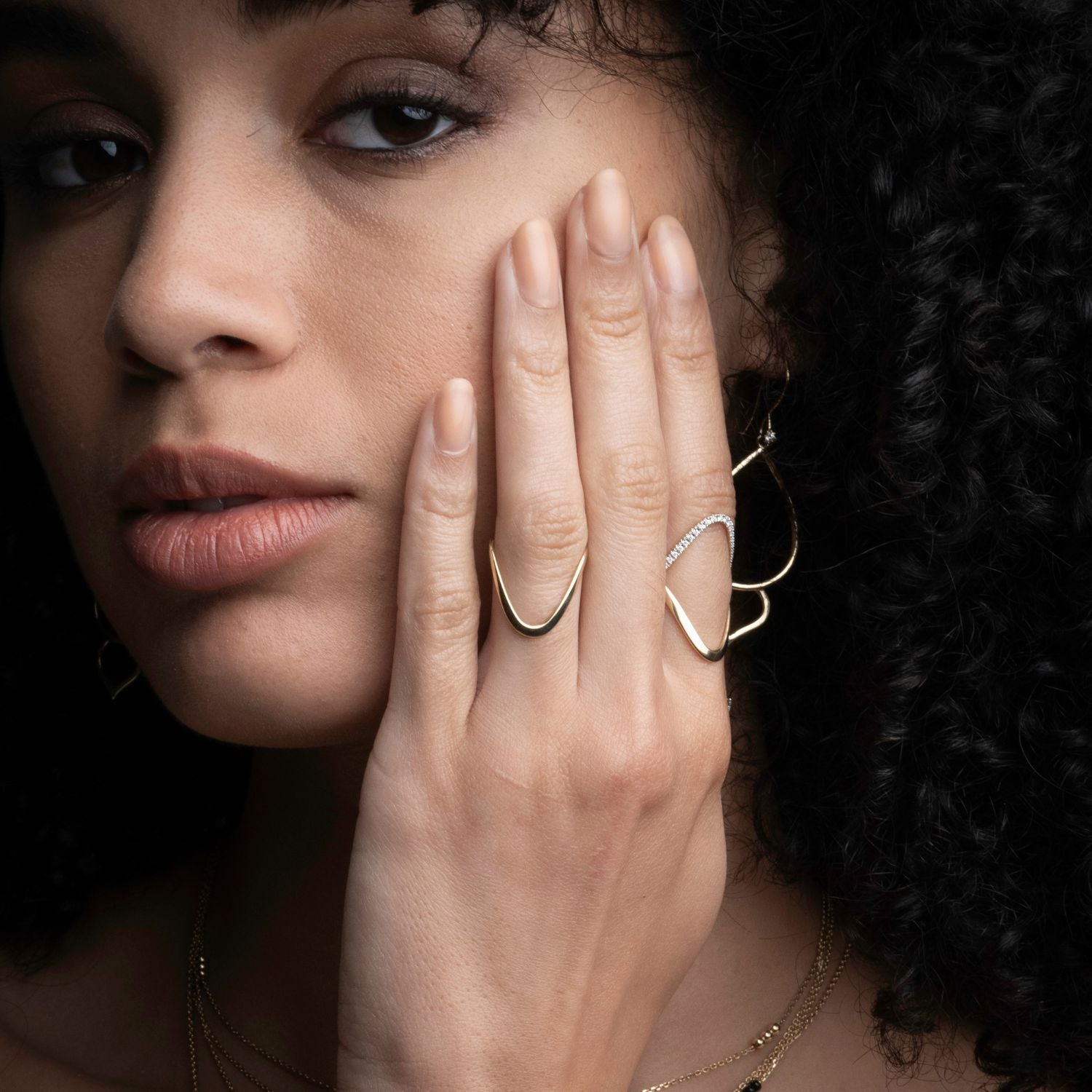Close-up of 14k yellow gold sculptural wave rings showing modern artistic design on hand