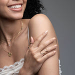 Woman wearing 14k yellow gold sculptural wave ring with layered necklaces from Confidence Collection